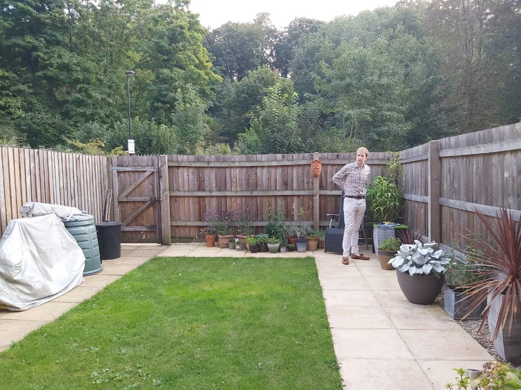 A patch of lawn surrounded by slabs and a high fence