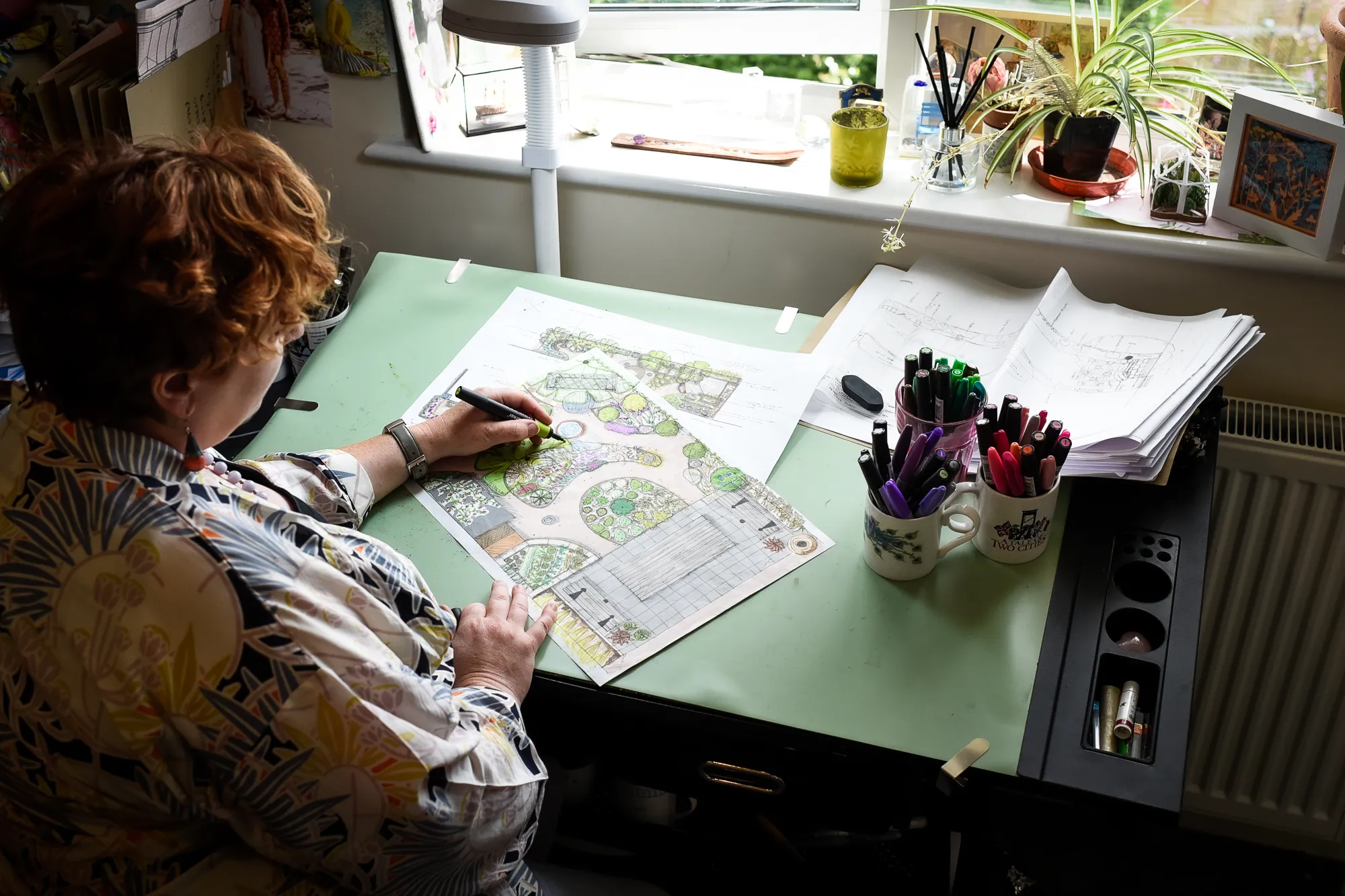 Charlotte sitting at a drawing board and colouring in a hand drawn design. Photo by Victoria Tapper